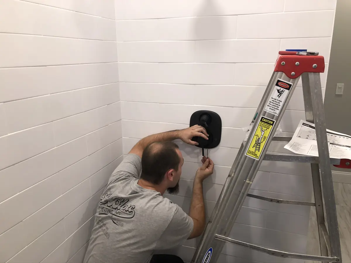 A.J. LeBlanc Heating technician installing a black shower valve trim on a subway tile shower wall in a Southern NH bathroom