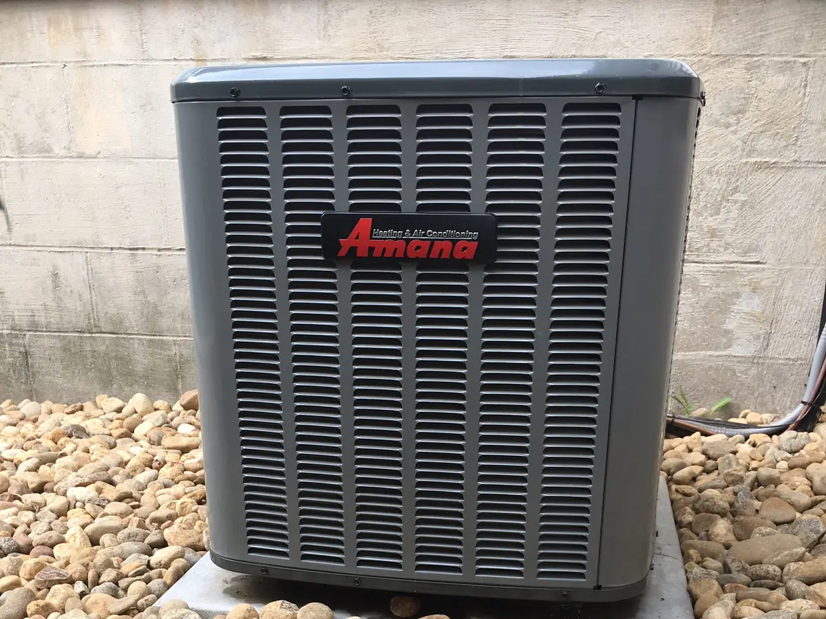 Amana central air conditioner condenser installed on a concrete pad with river rock landscaping by A.J. LeBlanc Heating in Southern NH