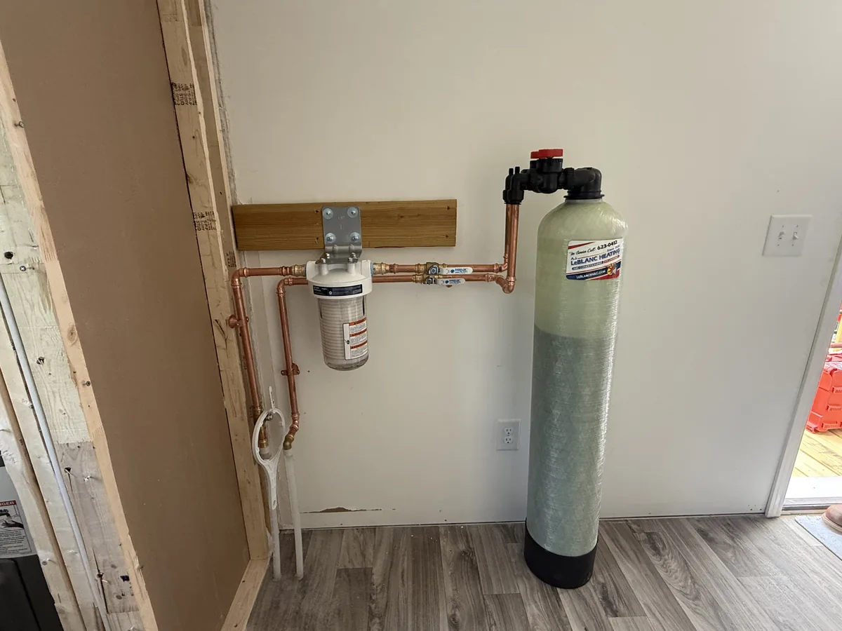 Arsenic treatment system for well water installed by A.J. LeBlanc Heating in a Southern NH home, with a clear sediment pre-filter and copper plumbing feeding a fiberglass arsenic-adsorption media tank