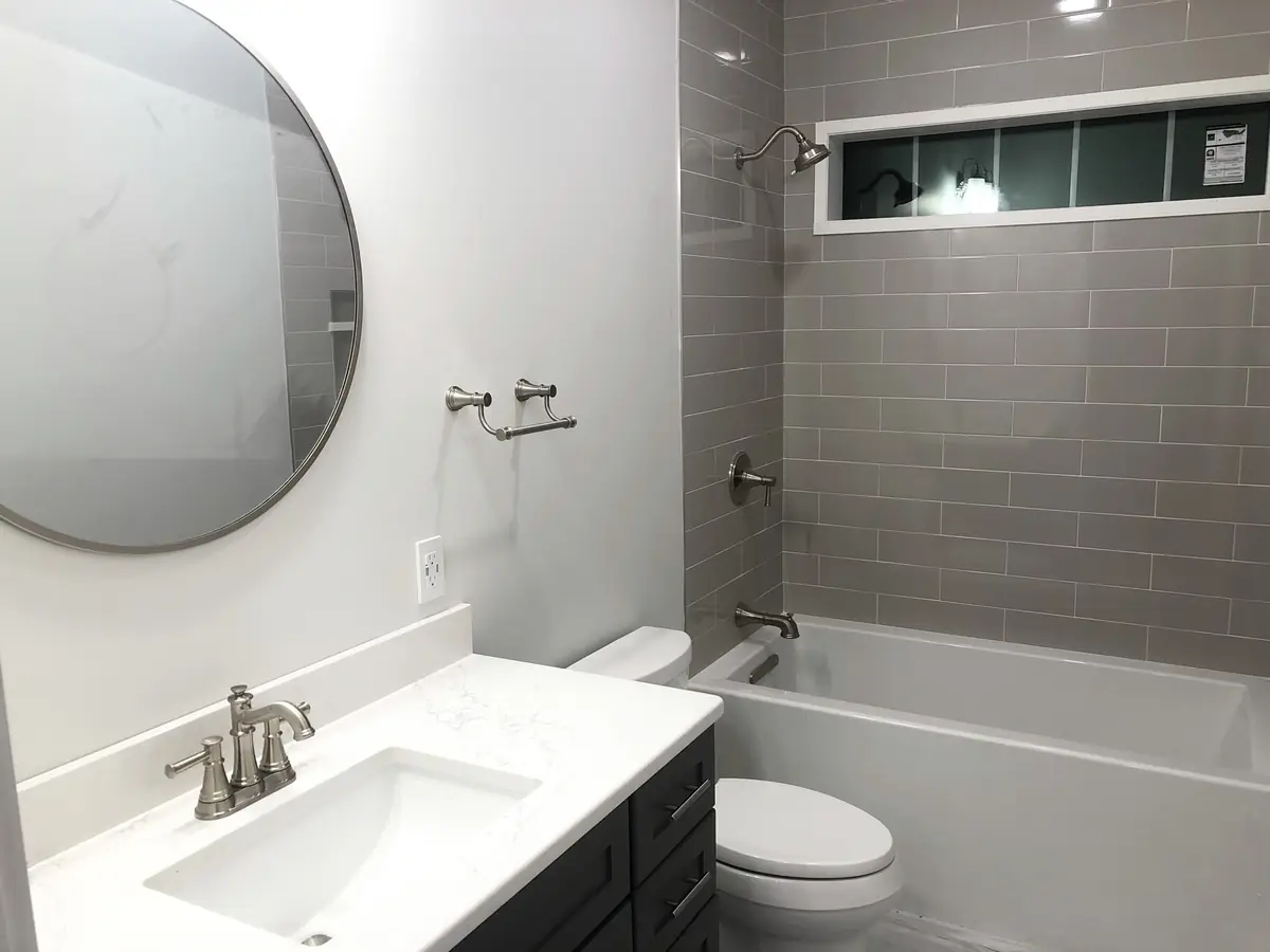 Bathroom remodel with brushed nickel fixtures, gray subway tile tub and shower, and white quartz vanity installed by A.J. LeBlanc Heating in a Southern NH home