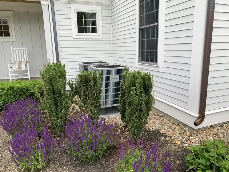 Pair of Bosch outdoor heat pump units with mature landscaping at a Southern NH home