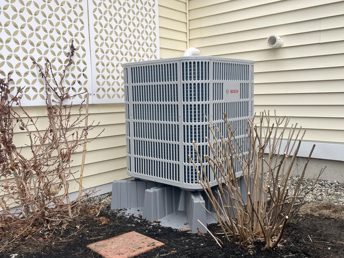 Bosch outdoor central heat pump condenser installed in residential landscape bed in Southern NH