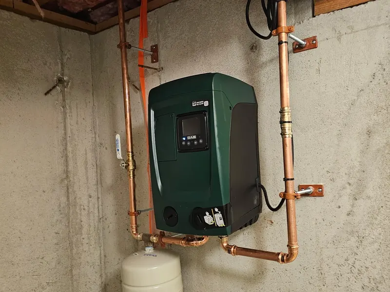 DAB green variable-speed constant pressure pump with LCD display, copper supply manifold, and small ProFlo expansion tank installed by A.J. LeBlanc Heating in a Southern NH home