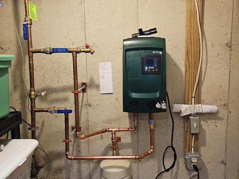 DAB green variable-speed constant pressure pump installed in a mechanical room with copper supply lines, expansion tank, and water heater nearby by A.J. LeBlanc Heating in a Southern NH home