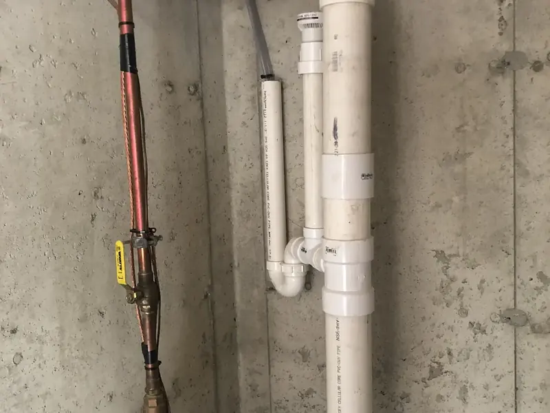 PVC drain stack and copper water main with water meter installed in a basement utility space by A.J. LeBlanc Heating in Southern NH