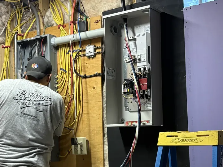 A.J. LeBlanc Heating electrician installing a whole-home automatic transfer switch that connects a standby generator to the electrical panel in a Southern NH home