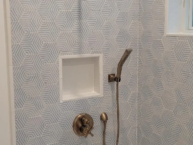 Walk-in shower with hexagon-pattern wall tile, brushed nickel rain shower head, thermostatic valve, niche, and handheld wand installed by A.J. LeBlanc Heating in a Southern NH home
