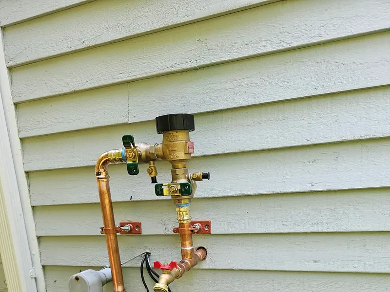 Brass irrigation backflow preventer with copper supply tap, T-fitting, and shut-off valves installed on the exterior of a Southern NH home by A.J. LeBlanc Heating