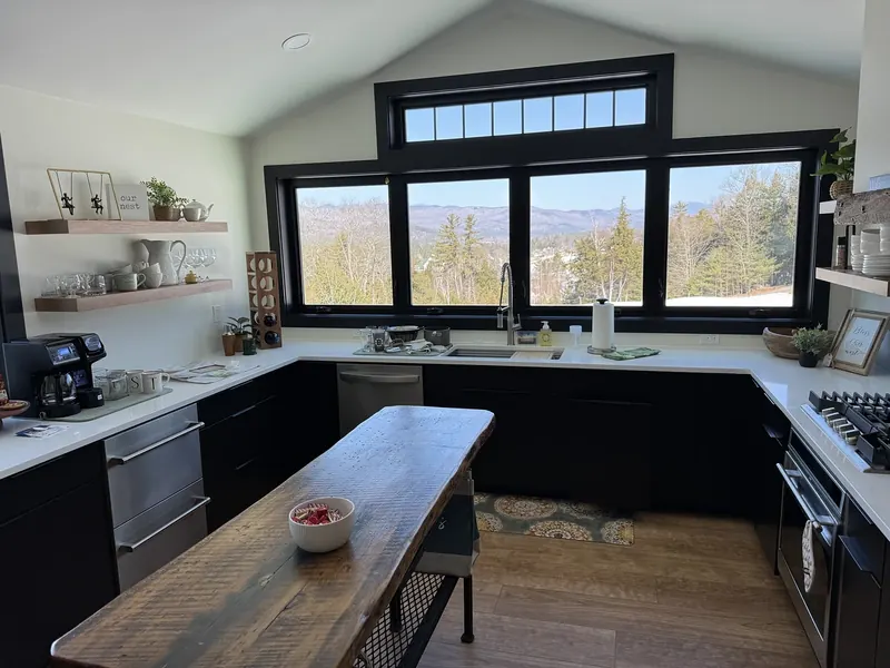 Full kitchen appliance install with stainless dishwasher, gas cooktop, and refrigerator beneath a panoramic mountain view window in a Southern NH home by A.J. LeBlanc Heating