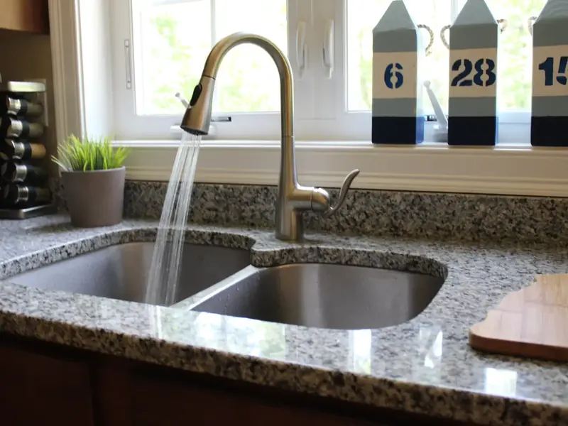 Chrome pull-down kitchen faucet on a granite counter with stainless steel double-bowl undermount sink installed by A.J. LeBlanc Heating in a Southern NH home