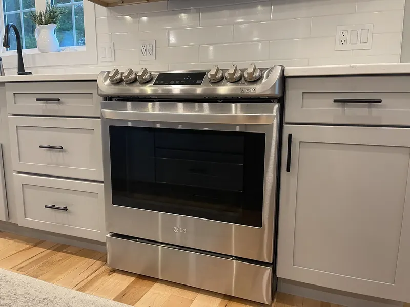 LG stainless steel slide-in electric range with smoothtop installed between gray shaker cabinets with subway tile backsplash by A.J. LeBlanc Heating in a Southern NH kitchen