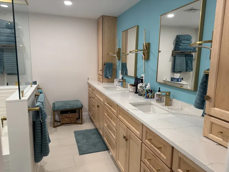 Long master bathroom with light wood double vanity, white marble counter, brass-framed mirrors and wall sconces, teal accent wall, brass fixtures, and freestanding tub installed by A.J. LeBlanc Heating in a Southern NH home