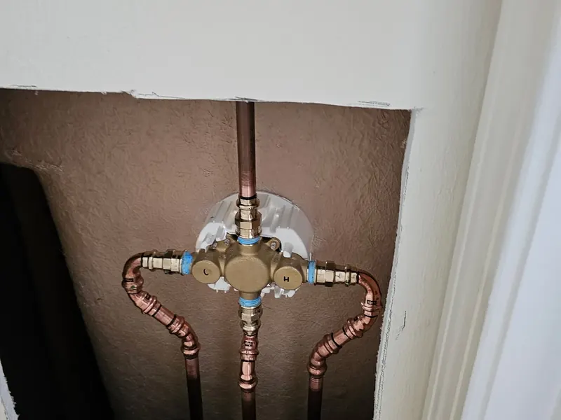 Behind-the-wall shower valve repair showing a new brass thermostatic mixing valve with freshly soldered copper hot, cold, shower riser, and tub spout supply lines by A.J. LeBlanc Heating in a Southern NH home