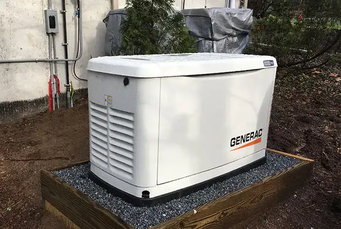Air-cooled Generac whole-home standby generator installed on a wood-framed gravel pad against vinyl siding in Southern NH by A.J. LeBlanc Heating