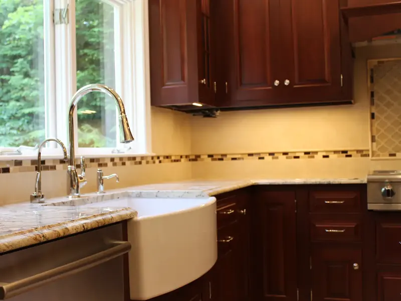 Traditional cherry kitchen with white farmhouse apron sink and chrome high-arc faucet installed by A.J. LeBlanc Heating in a Southern NH home