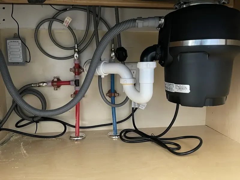 Under-sink kitchen plumbing with garbage disposal, supply lines, and P-trap installed by A.J. LeBlanc Heating in a Southern NH home