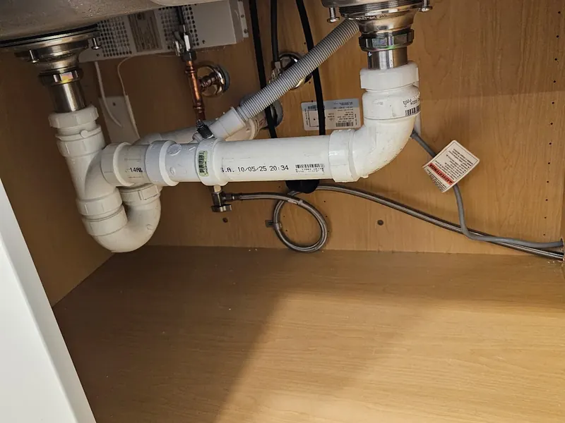 Under-sink plumbing replacement with new white PVC P-trap, chrome basket strainers, braided dishwasher drain hose, and fresh shut-off valves by A.J. LeBlanc Heating in a Southern NH kitchen