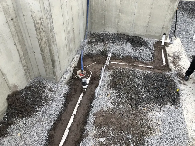 Under-slab PVC drain lines and floor drain riser set in a gravel base inside a new construction foundation before the concrete pour, by A.J. LeBlanc Heating in Southern NH