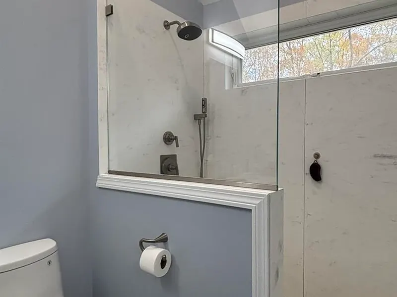 Walk-in marble shower with glass divider wall, shower head with handheld wand, and clerestory window installed by A.J. LeBlanc Heating in a Southern NH home