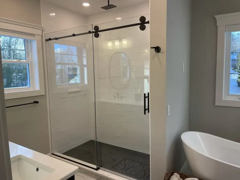 Walk-in subway tile shower with black framed glass barn door and freestanding tub installed by A.J. LeBlanc Heating in a Southern NH home