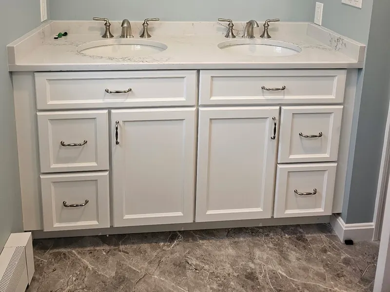 White shaker double vanity with brushed nickel widespread faucets, marble counter, and marble tile floor installed by A.J. LeBlanc Heating in a Southern NH bathroom